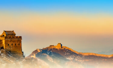 Great Wall of China winding over rocky hills at golden hour, with snow-dusted rocks and a blue-orange sky