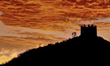 the great wall, Beijing, chinatravel, Silhouette of a hill with a ruined castle tower against a dramatic orange sunset sky.