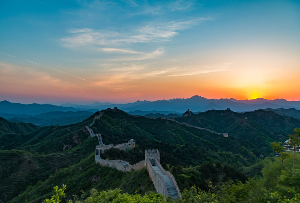 Sunset lights up the Great Wall winding over green hills and watchtowers at dusk.
