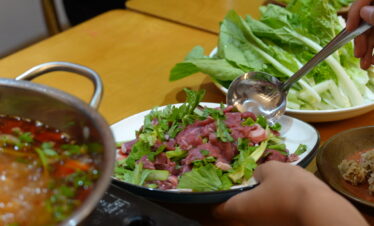 guizhou food, china, china tour, Plate of thin beef and fresh greens (cilantro and lettuce) ready for hot pot, with a hand using a ladle nearby.