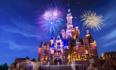 Shanghai-Disneyland-Castle, china, chinaexplorertour, Castle illuminated at night with colorful fireworks bursting overhead, set on a rocky base and blue sky.
