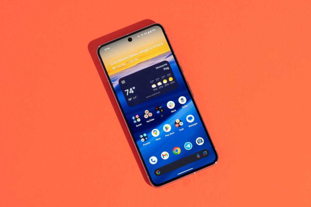Smartphone tilted on an orange background showing home screen with widgets and app icons visible on the display