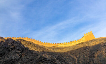 the great wall, Beijing, chinatravel, Curved stone fortress wall with crenellations along a rocky hillside under a clear blue sky
