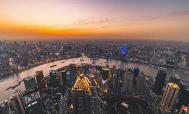 Shanghai, A Guide to Chinese Accommodation: Hotels, Hostels, and More, chinaexplorertour, Aerial view of Shanghai skyline at sunset with the Huangpu River and illuminated skyscrapers, including the Oriental Pearl Tower in the center.