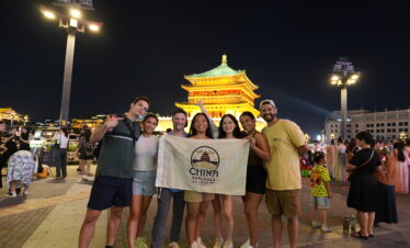 Xi'an Bell Tower with China Explorer Tour, china, china tour, Group of friends posing with a banner that reads 'China Explorer Tour' in front of a lit traditional pagoda at night.