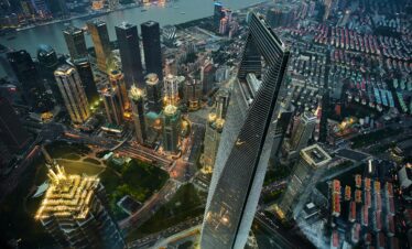 shanghai, china, china tour, Aerial view of Shanghai's skyline with skyscrapers along a river and a distinctive triangular glass tower at center. Avoids