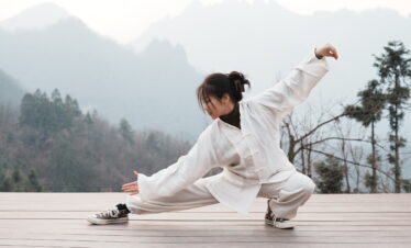 Wudang, shiyan, hubei, china tour, Person in a light beige martial arts outfit performing a low stance on a wooden deck with misty mountains in the background
