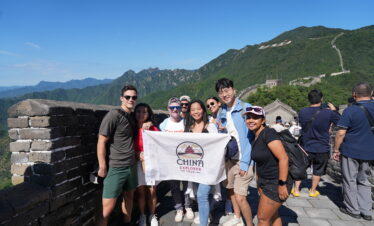 Mutianyu Great Wall, Beijing, Chinatravel, Group of diverse tourists posing with a China Explorer Tour banner on the Great Wall, blue sky and green mountains in the background.