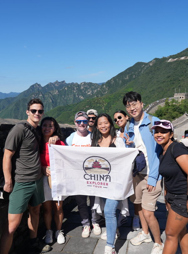 Mutianyu Great Wall, Beijing, Chinatravel, Group of diverse tourists posing with a China Explorer Tour banner on the Great Wall, blue sky and green mountains in the background.
