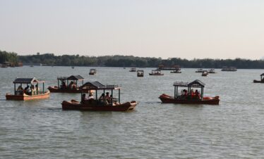 Summer Palace, beijing, china, chinatrip, Multiple wooden boats with canopies carrying groups of people on a calm lake, with a tree-lined shore in the distance under a clear sky.
