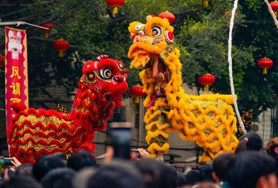 Celebrate the Chinese New Year with China Explorer Tour, Traditional lion dance in yellow and red costumes performing for a crowd under red lanterns at a street festival.