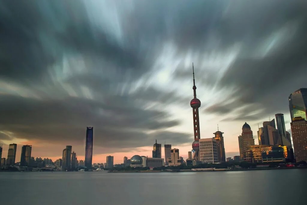 Shanghai City Tours, china tour, Shanghai skyline across the Huangpu River at sunset, with the Oriental Pearl Tower amid tall modern buildings and a cloudy sky