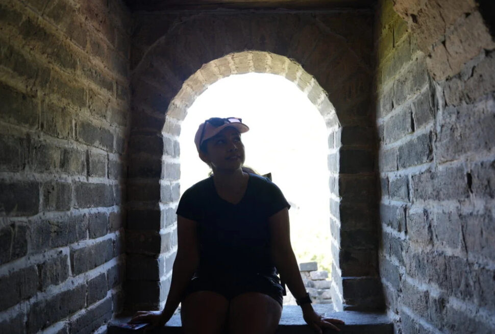 the great wall, Why Indian Travelers Love China Explorer Tour, Person wearing a cap sits on a stone ledge inside a dark brick archway, with bright daylight visible outside behind them (backlit scene).