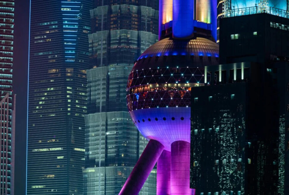 Shanghai City Tours, china tour, Night cityscape at night featuring the illuminated Oriental Pearl Tower with purple-blue lights among tall glass buildings in Shanghai .