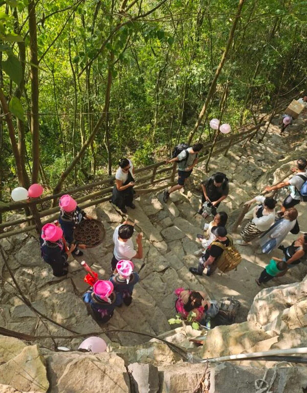 Guizhou: Your Guide to Shuicheng County, china tour, Group of people gathered on a stone outdoor stairway in a forest, some wearing pink hats, with balloons tied to the railing.