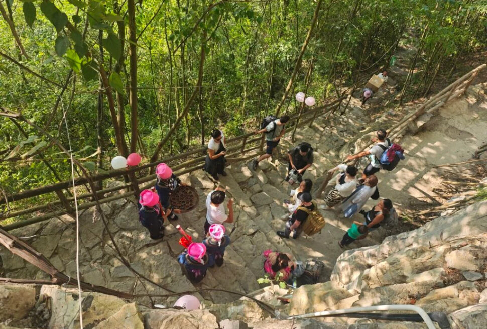 Guizhou: Your Guide to Shuicheng County, china tour, Group of people gathered on a stone outdoor stairway in a forest, some wearing pink hats, with balloons tied to the railing.