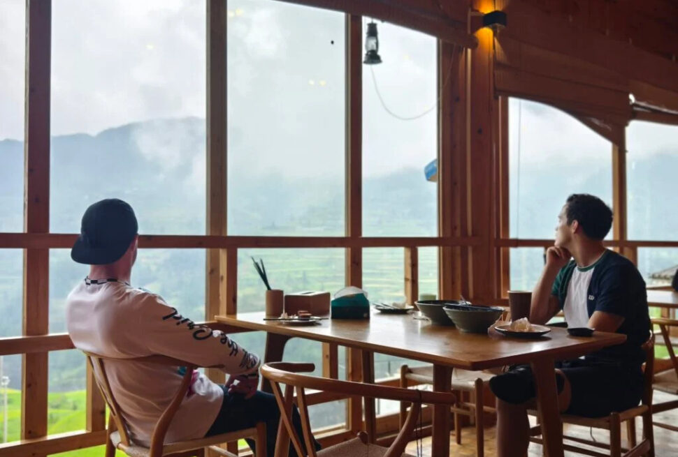 guizhou, china, china tour, Two men sit at a wooden table in a bright cafe, overlooking misty mountains through large windows.