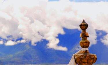 Tibet, china, china tour, Close-up of a weathered wooden finial with a white cloth tied around, set against a blue sky and distant mountains.