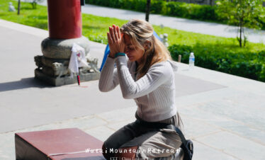 wutai retreat, shanxi, chinatrip, Woman kneeling in a peaceful outdoor setting, hands pressed together in prayer, eyes closed, with a retreat banner visible at the bottom.