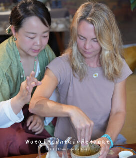 wutai retreat, shanxi, chinatrip, Two women participate in a tea ceremony; one guides the other as they whisk tea powder in a bowl together in a cozy setting.