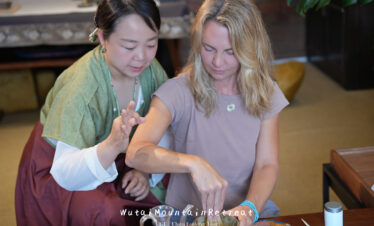 wutai retreat, shanxi, chinatrip, Two women participate in a tea ceremony; one guides the other as they whisk tea powder in a bowl together in a cozy setting.