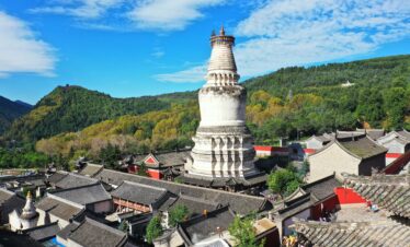 Mount Wutai, shanxi, china, china tour, White Buddhist stupa rising above a Chinese temple complex with gray tiled roofs and green hills in the background.