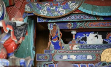 Foguang Temple, Mount Wutai, shanxi, china, china tour, Stacked, ornately painted wooden panels from a temple or shrine, featuring blue, green, and red geometric and wave patterns with a small carved warrior figure in blue and orange standing among them
