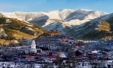 Mount Wutai, shanxi, china, china tour, Snowy mountain town with red buildings and a white pagoda in the foreground, snow-covered slopes in the background under a blue sky.