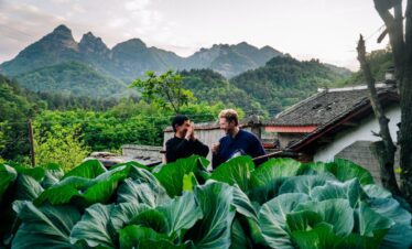 5-Day Wudang Mountain Tai Chi Retreat, hubei, china tour, Two men chat in a rural vegetable garden with oversized leafy greens in the foreground and mountains and traditional houses in the background.