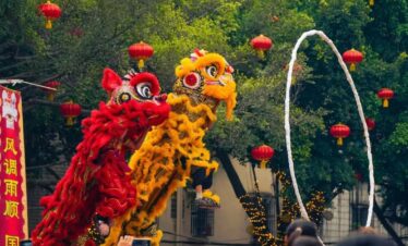 Chinese New Year Adventure jorney, southern china, chinatrip, Two colorful dragon/demon dancers perform a lion-like creature dance with a white hoop in front of a crowd at a festival, red lanterns overhead.