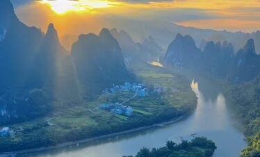 yangshuo, guangxi, china, chinatrip, Sunset over a winding river surrounded by towering karst mountains and a small village at riverbank.