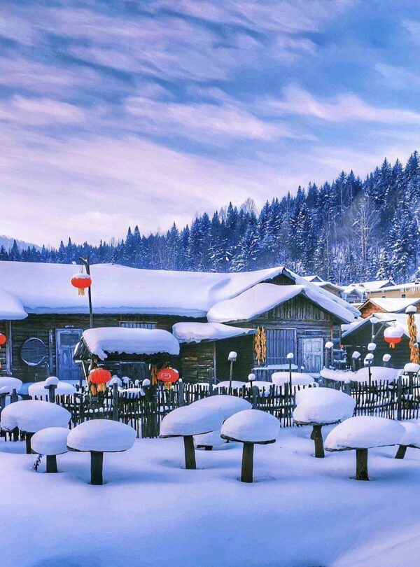 Enchanting Winter Wonderland: 3-Day Journey Through Harbin: China's Snow Kingdom, chinatrip, Snow-covered village with wooden houses and bright red lanterns along a snowy path. Nearby pine trees and hills in the background winter scene.