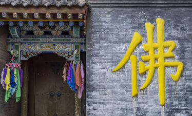 Pushou Temple, Mount Wutai, shanxi, china, china tour, Bright yellow Chinese character painted on a weathered gray brick wall beside a richly painted temple doorway with hanging colorful cloths.