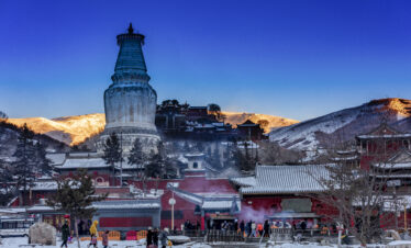 Snow-dusted White Pagoda under a Golden Mountain Sunrise, Mount Wutai, shanxi, china, china tour, Snow-covered temple complex with a towering white stupa in the foreground and snow-dusted rooftops, set against sunlit hills at dusk.