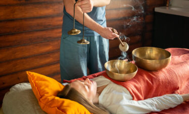 Tibetan singing bowls treatment in spa salon, Mount Wutai, shanxi, china, china tour, Person lying on a bed with orange pillow, eyes closed, as a practitioner plays brass singing bowls for sound therapy.