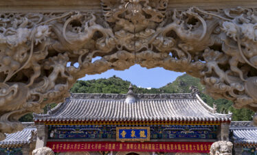 Longquan Temple, Mount Wutai, shanxi, china, china tour, Ornate stone dragon archway framing a temple roof with mountains in the background