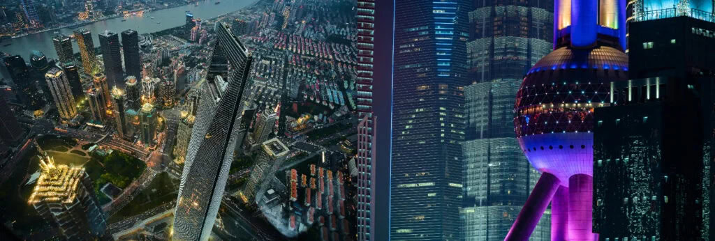 shanghai, china, chinaexplorertour, Nighttime aerial view of a densely built city with glowing skyscrapers and a purple-lit futuristic tower.