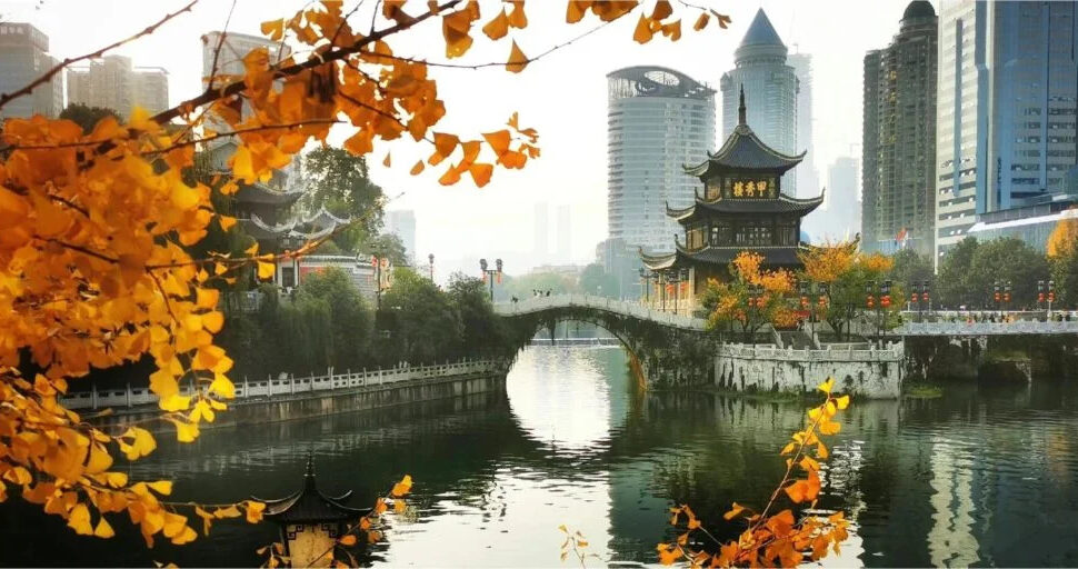 jiaxiu pavilion, guiyang, guizhou, china, chinaexplorertour, Autumn orange leaves frame a lake with a curved stone bridge and a traditional pagoda in a city park.