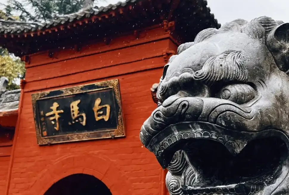 white horse temple, luoyang, henan, china tour, Red temple entrance with a carved stone guardian lion in the foreground and a gold-inscribed plaque on the wall.