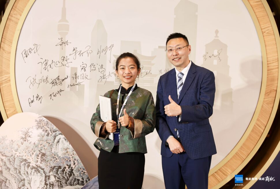 china explorer tour, china travel agency, china tour, Two professionals pose with thumbs up in front of a round backdrop featuring a city skyline and signatures.