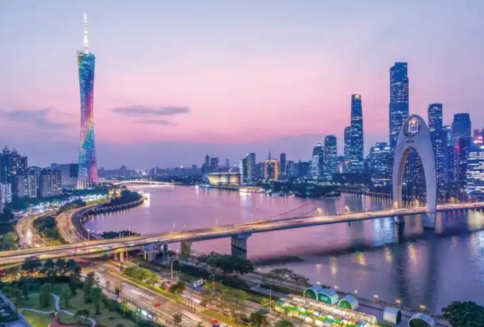 guangzhou, china, chinaexplorertour, A nighttime city skyline with a colorful-lit tower, a curved arch bridge over a river, and bright high-rise buildings reflecting on the water.