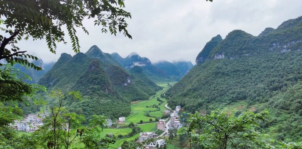 guizhou, chinatravel, Lush green valley with a winding road and small village nestled among towering karst mountains.