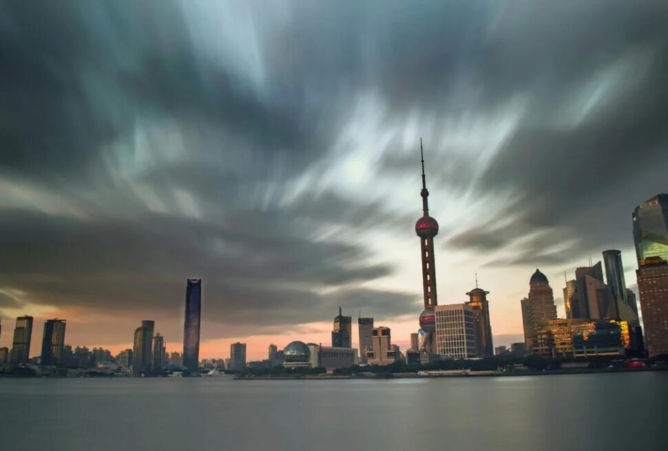 shanghai, chinatravel, Shanghai skyline at sunset with the Oriental Pearl Tower rising above the river and dramatic clouds overhead in the sky's warm glow.