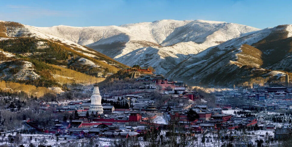 wutai mountain, wutai, chinatravel, Snow-dusted mountain village with a white stupa-like tower and red-roofed buildings in a valley.