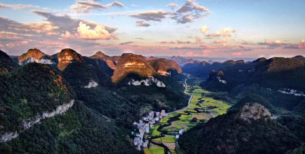 guizhou, chinatravel, Winding river valley with patchwork green fields and limestone mountains at sunset, a small village at the valley floor.