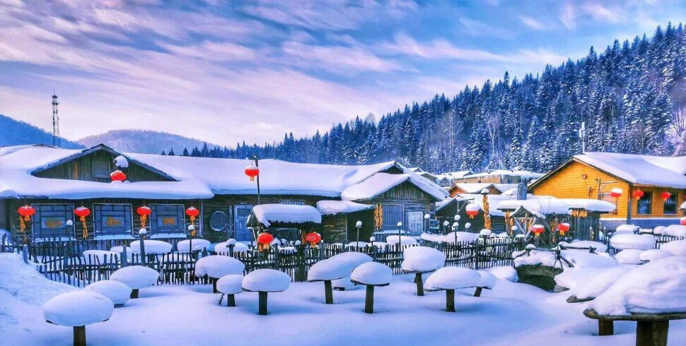 harbin, snow town, chinatravel, Snowy village scene with wooden cabins, red lanterns, and a snow-covered courtyard set against a forested hillside.
