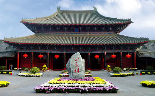 the prefecture of kaifeng, henan, chinatrip, Traditional Chinese temple with red lanterns and a central stone stele inscribed in Chinese characters, surrounded by flower beds.