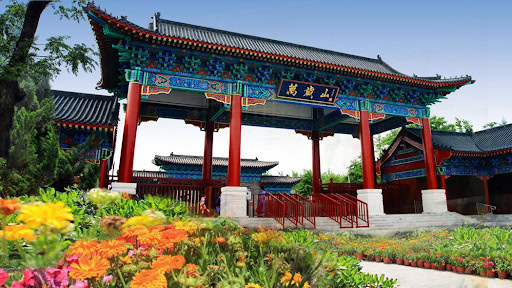 the song dynasty of kungfu city, kaifeng, henan, chinatrip, Colorful Chinese gate with red columns and ornate blue-green roof, framed by blooming flowers in the foreground.