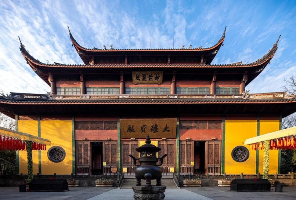 Lingyin Temple, hangzhou, zhejiang, china tour, Traditional Chinese temple with yellow walls and curved roofs, central incense burner in a stone courtyard under a blue sky