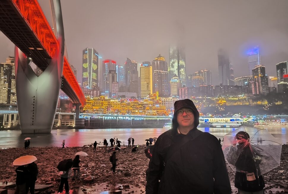 Qiansimen Jialing River Bridge, Hongya Cave, chongqing, chinatrip, Night city skyline at night with a bright red-lit bridge, misty skyline, and people on a rocky shore holding umbrellas in the rain.